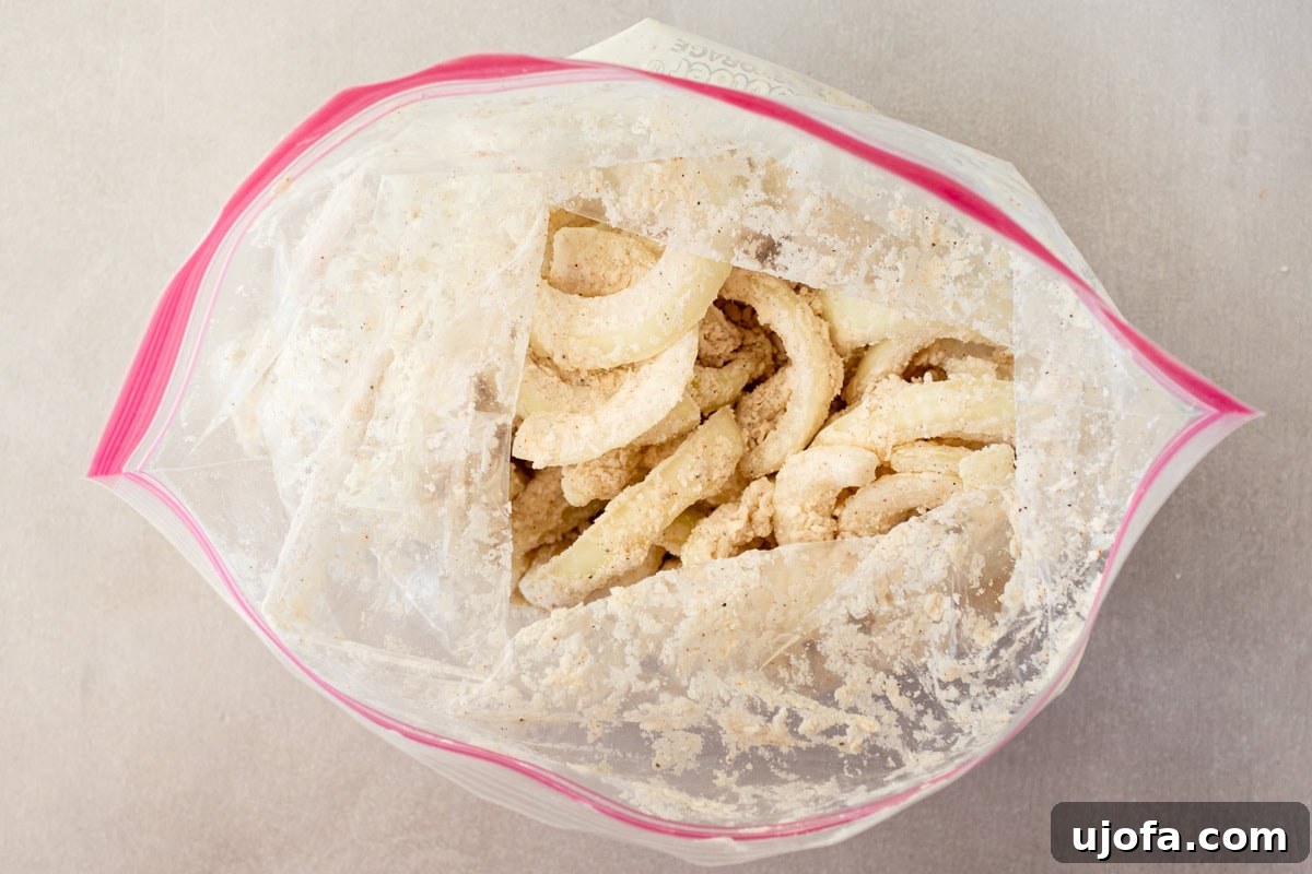 Onion slices, having been tossed in the seasoned gluten-free flour mixture, are visible inside a zip-top bag, coated and ready to fry.