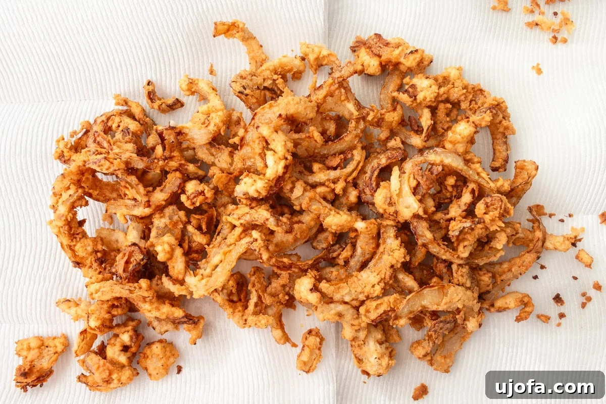 Freshly fried gluten-free onions resting on a paper towel-lined tray, ready for a final sprinkle of salt.