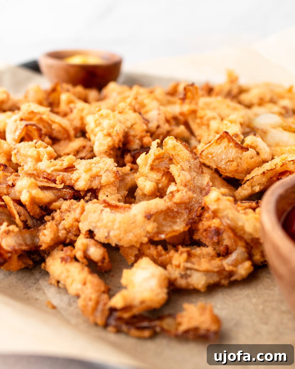 Side view of a generous portion of golden gluten-free fried onions piled on a tray, showcasing their irresistible crispiness.