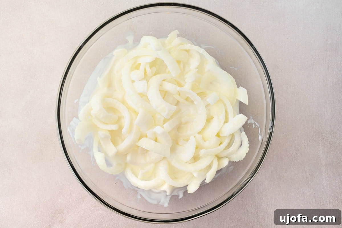 Sliced onions soaking in buttermilk in a mixing bowl, ready for the next step of the recipe.