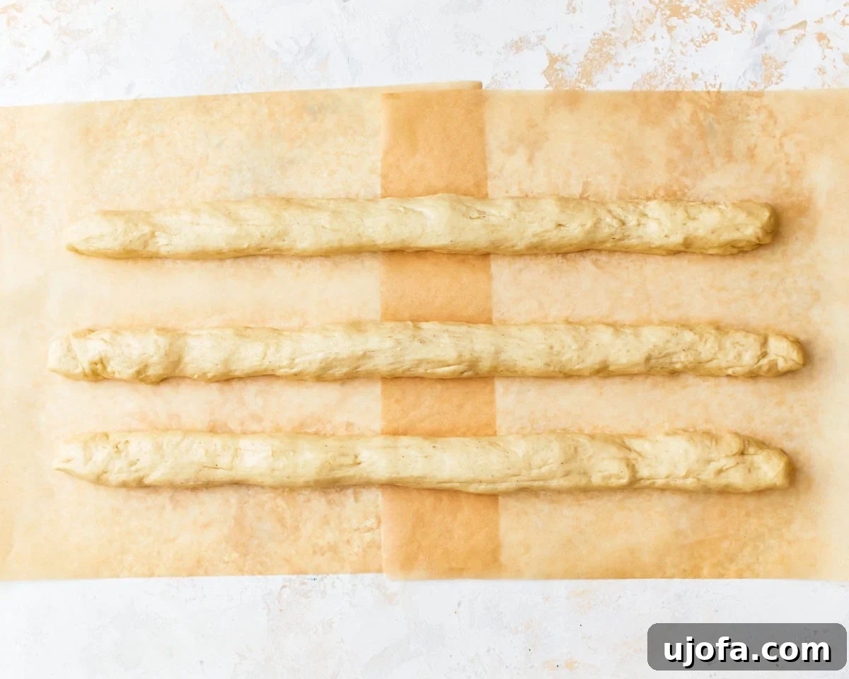 Gluten-free challah bread dough divided into three and rolled into a long rope shape on parchment paper.
