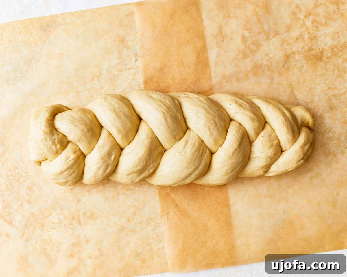 Gluten-free challah bread dough shaped into a braided loaf on a piece of parchment paper.