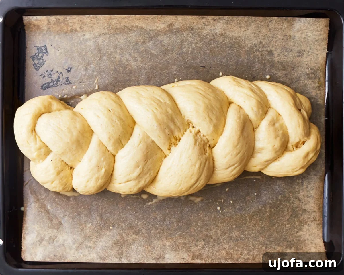 Gluten-free challah bread dough shaped into a braided loaf on a parchment lined baking sheet.