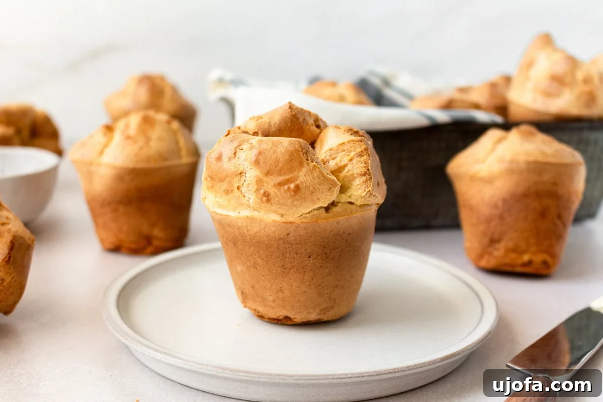 Side view of a perfectly risen gluten-free popover on a white plate, showcasing its golden crust and airy interior.