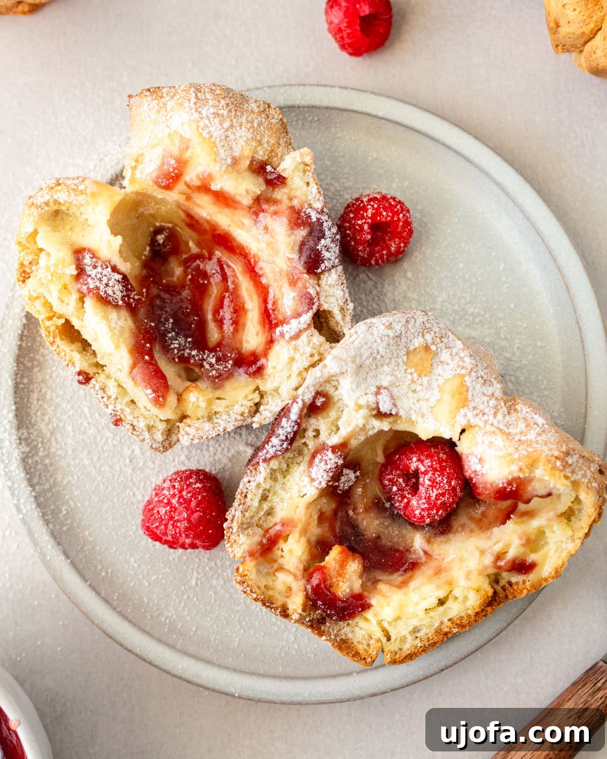Overhead view of a gluten-free popover cut in half, revealing its airy interior, served on a white plate with fresh raspberries and powdered sugar.