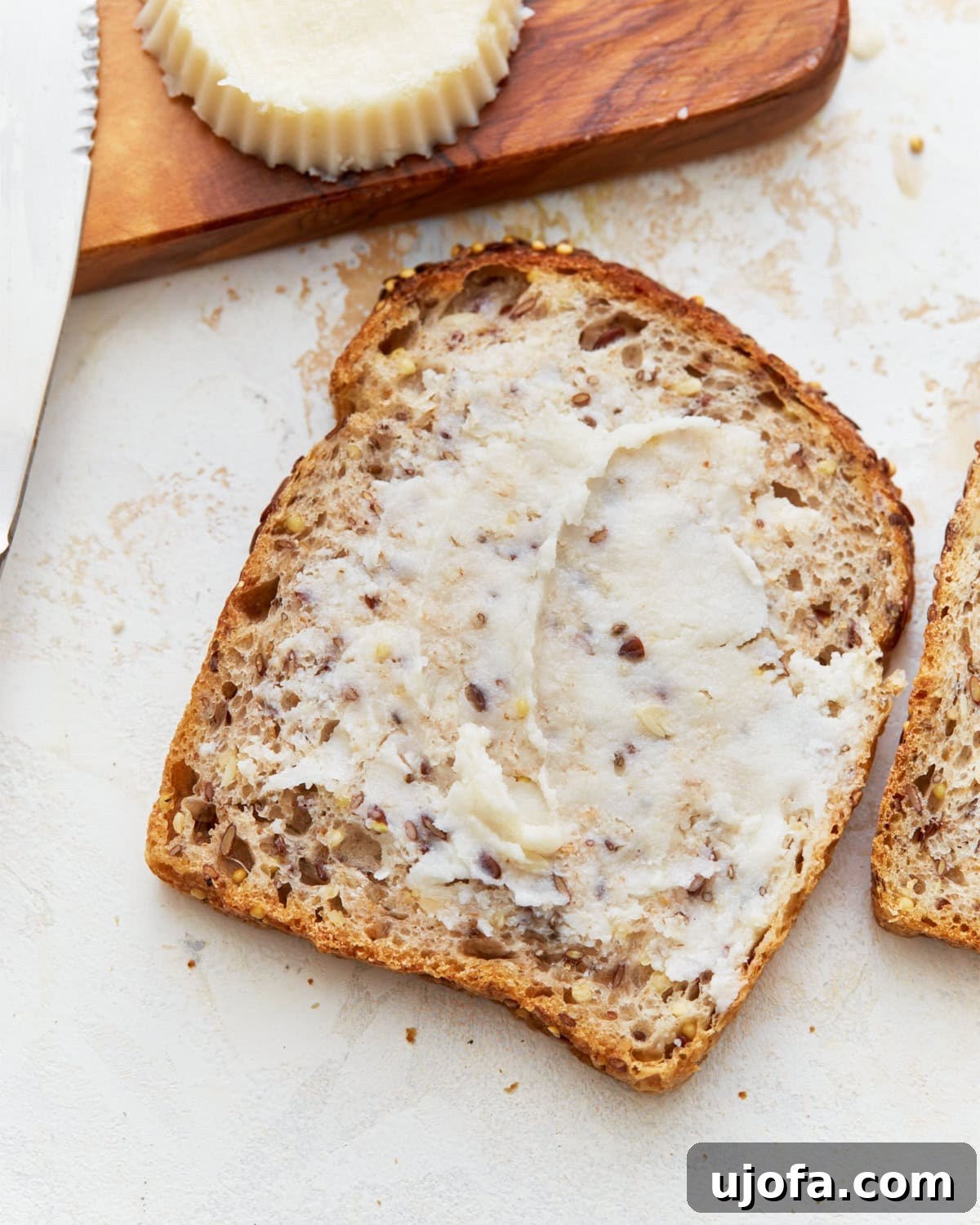A slice of golden-brown toast generously topped with creamy homemade vegan butter, resting on a rustic wooden cutting board next to a small dish of the butter.