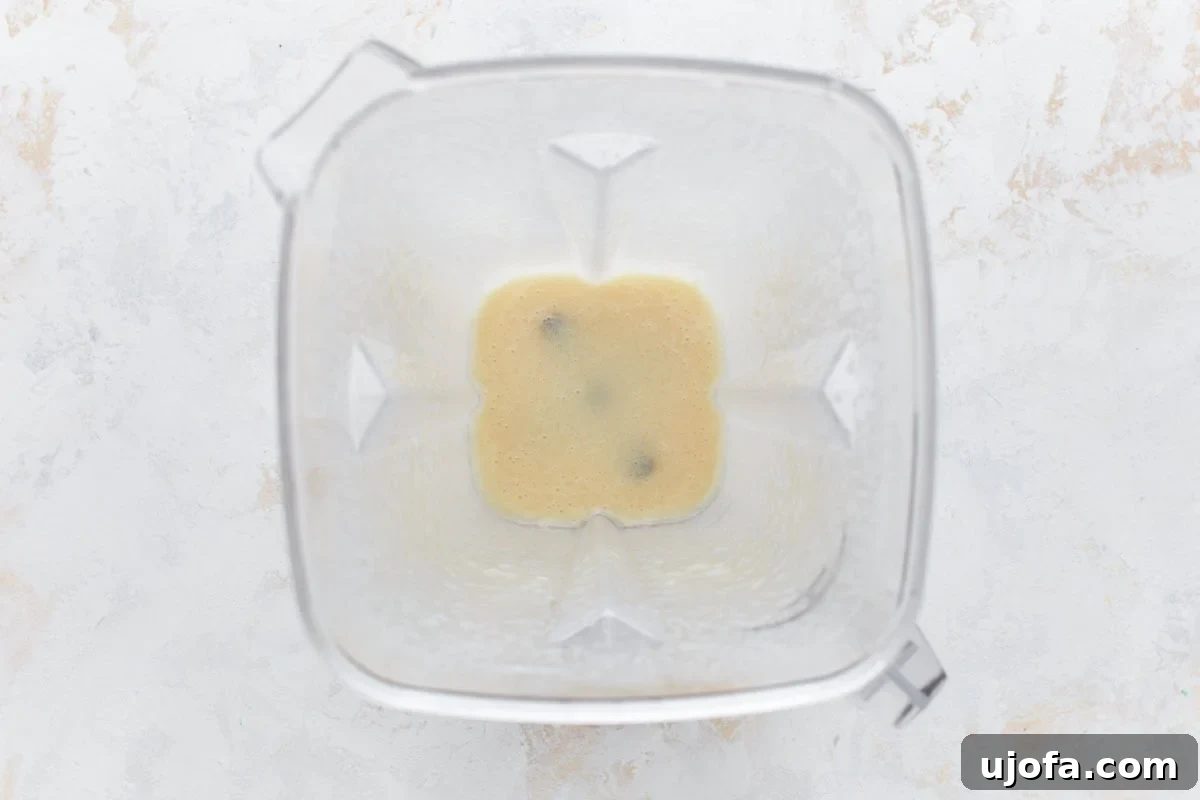 An overhead view of a blender filled with all the liquid ingredients for vegan butter: refined coconut oil, canola oil, unsweetened almond milk, apple cider vinegar, nutritional yeast, and salt, ready to be blended into a smooth mixture.