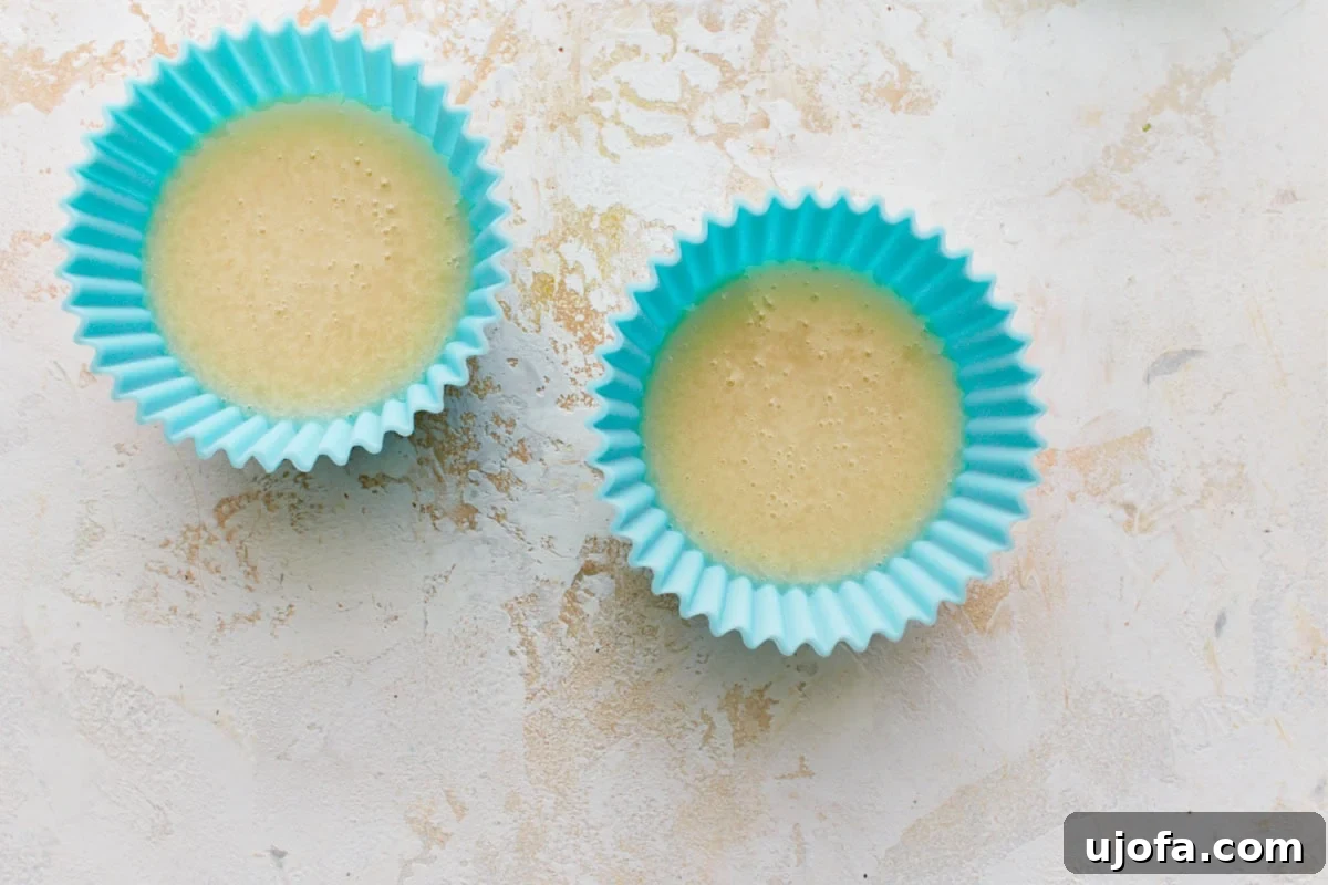 Two silicone cupcake molds, neatly filled with the creamy liquid vegan butter mixture, ready for chilling. This shows a convenient way to portion the butter as it sets.