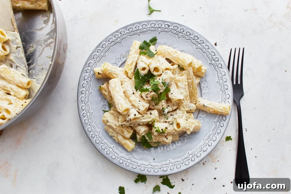 Decadent Gluten Free Boursin Pasta 5 A overhead view of a plate of gluten-free Boursin cheese pasta with a parsley garnish and a fork to the right