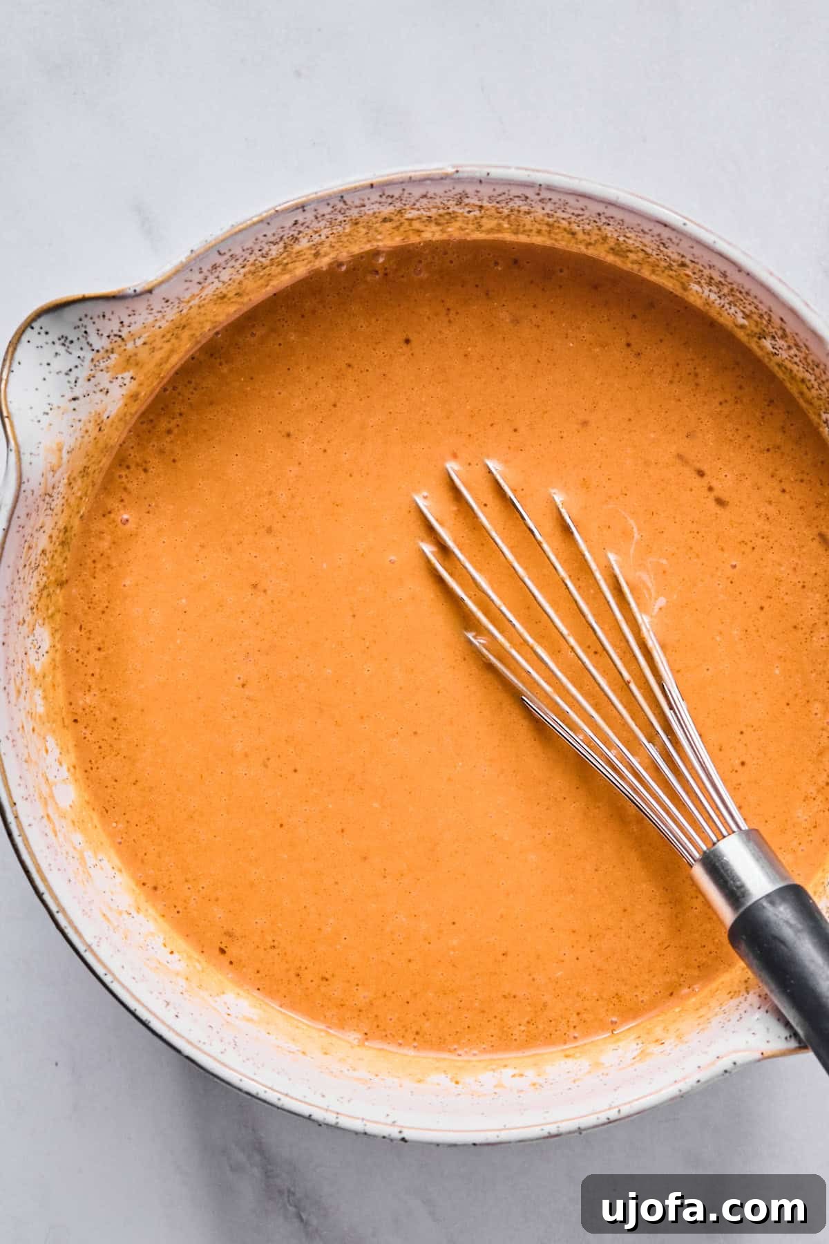A bowl filled with a vibrant red Thai curry sauce, being smoothly whisked to combine all the ingredients.