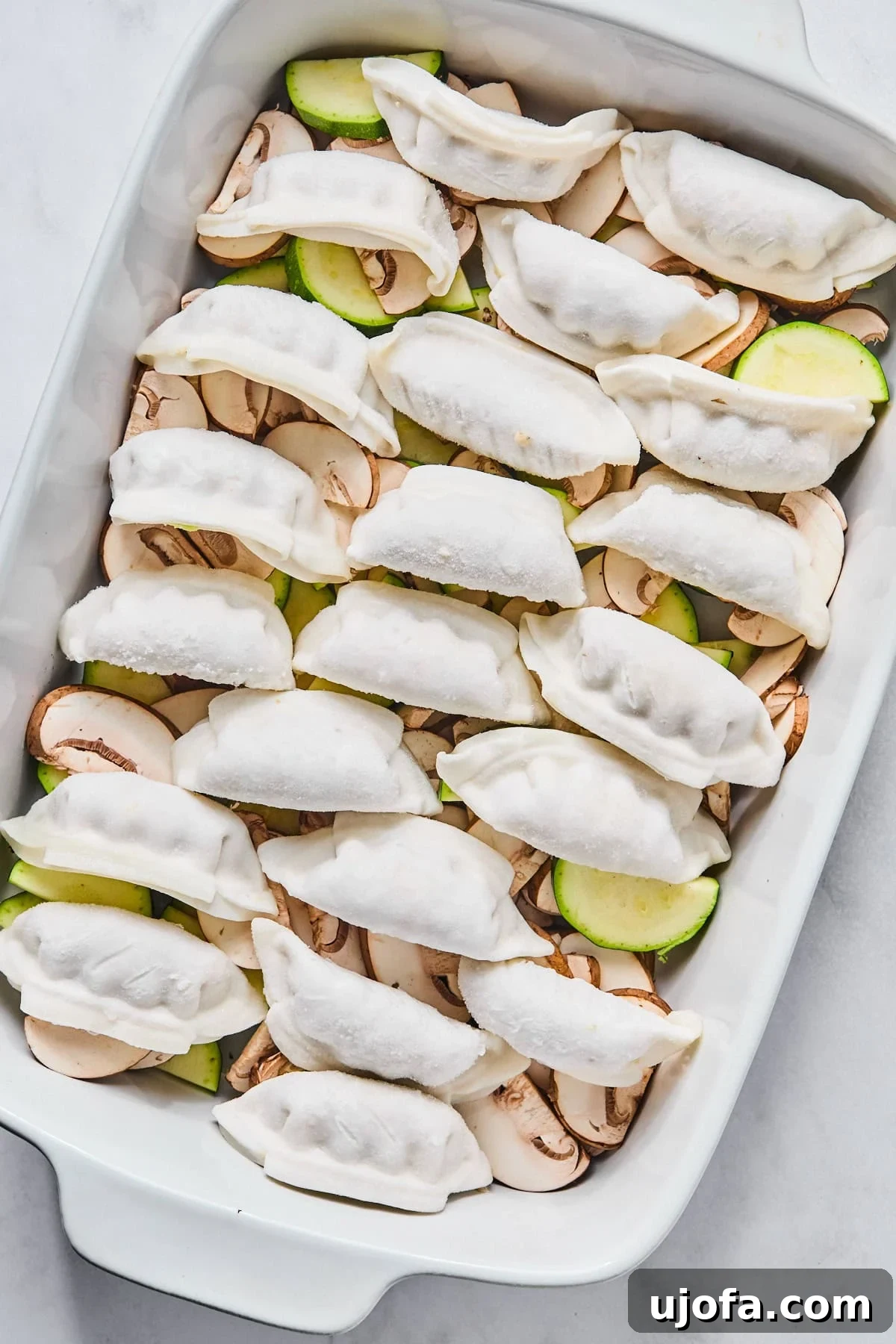 Frozen gluten-free dumplings carefully arranged in a single layer on top of the vegetables in a baking dish.