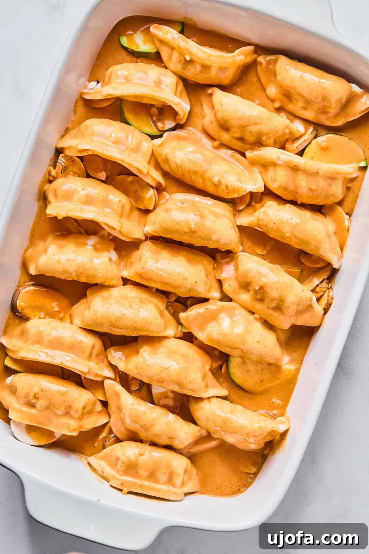 A casserole dish filled with dumplings and vegetables, generously covered with a rich red curry sauce, ready for baking.