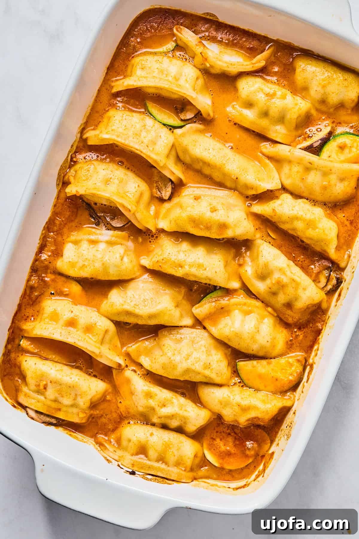 Baked potstickers simmering in a bubbling red sauce within a casserole dish, having just been uncovered during the baking process.