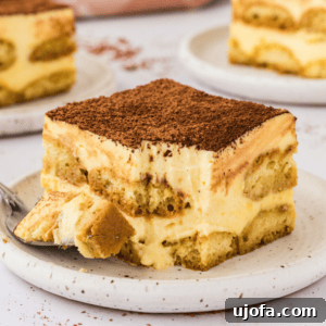 piece of tiramisu on white plate with more plates in the background