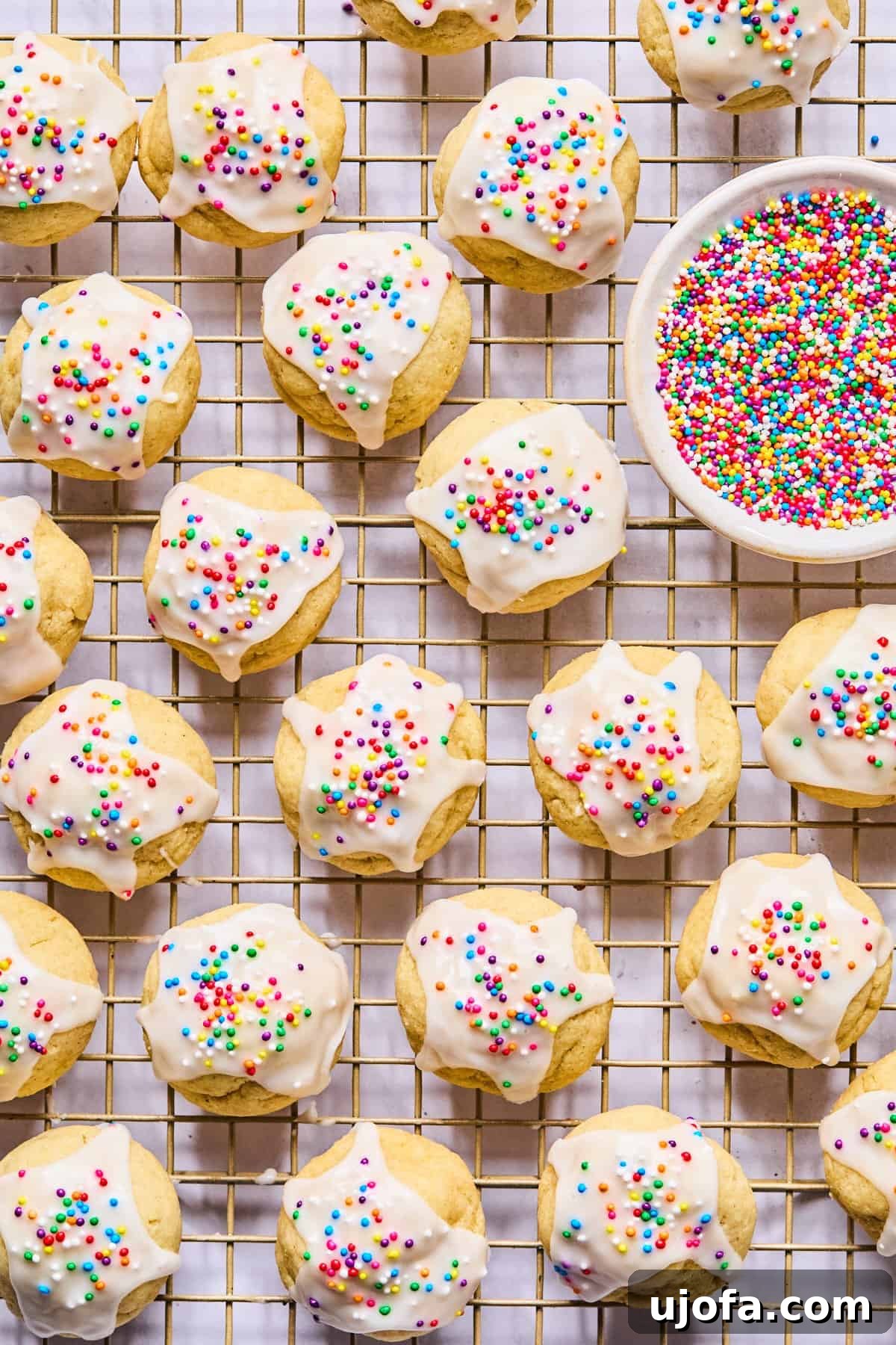 Sweet Traditions: Gluten-Free Italian Wedding Cookies 12 Gluten free Italian wedding cookies on a wire cooling rack with a nesting bowl of rainbow sprinkles next to them, ready for glazing.