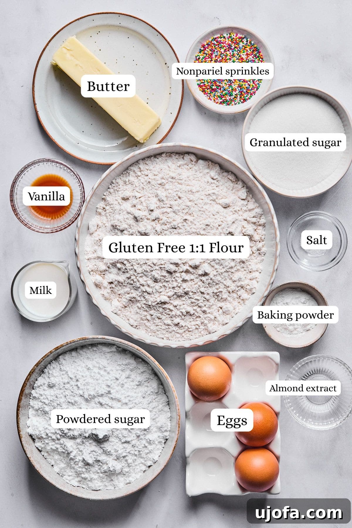 Sweet Traditions: Gluten-Free Italian Wedding Cookies 3 Gluten free Italian wedding cookies ingredients labeled and laid out on a light gray countertop, including flour, sugar, butter, eggs, and extracts.