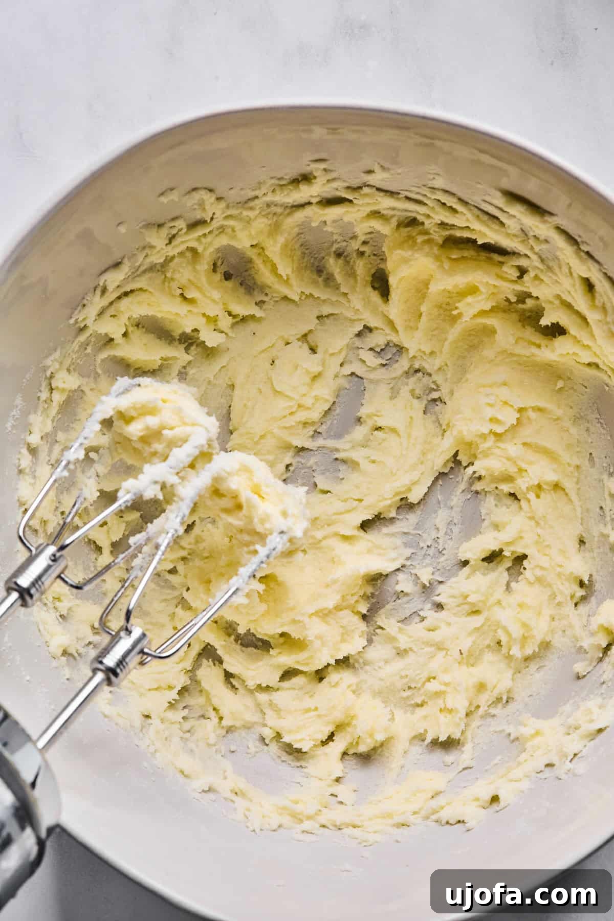 Sweet Traditions: Gluten-Free Italian Wedding Cookies 5 A large mixing bowl with softened butter and granulated sugar creamed together, with a handheld electric mixer resting on the bowl.