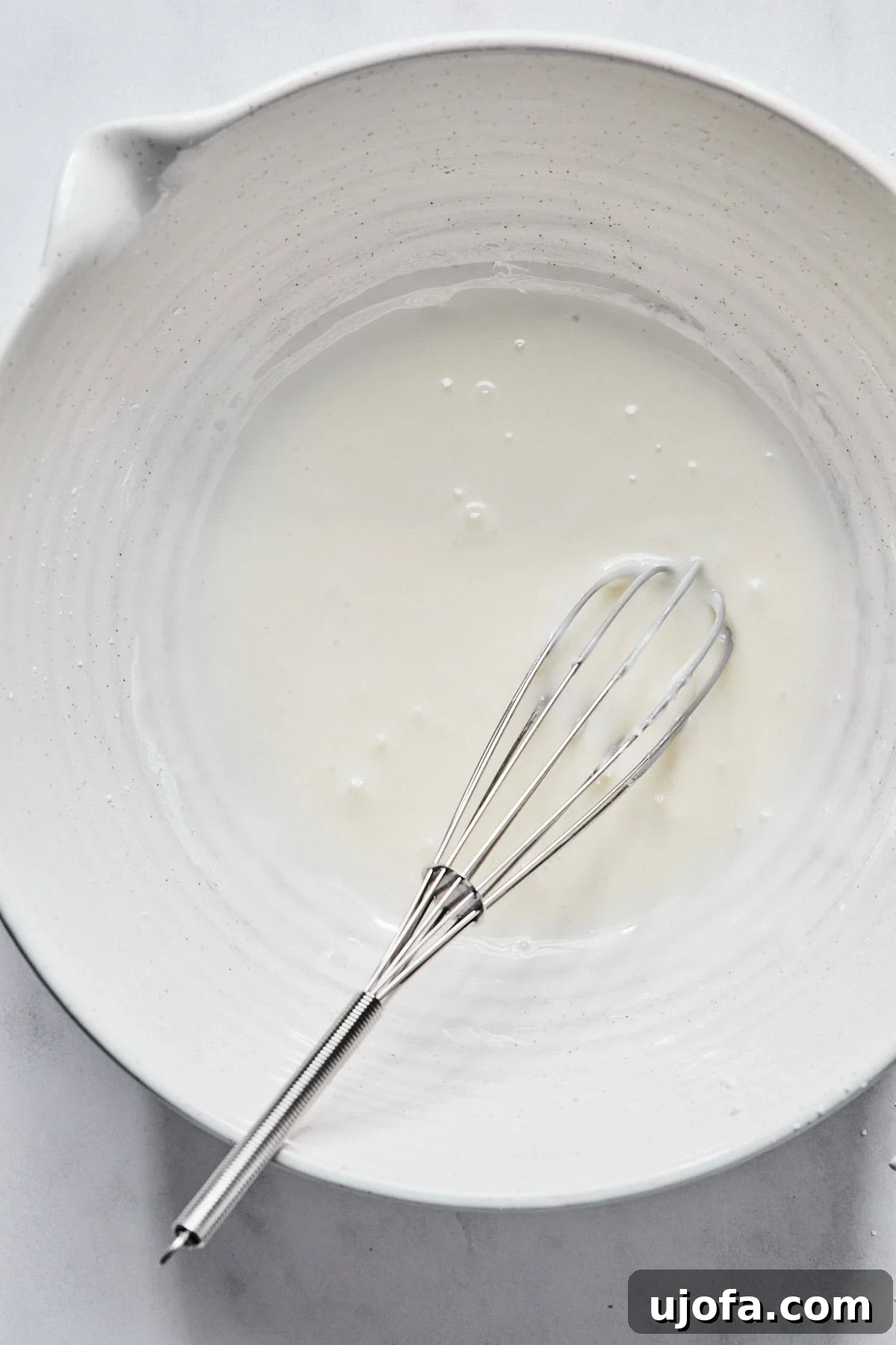 Sweet Traditions: Gluten-Free Italian Wedding Cookies 9 Almond glaze in a medium white bowl with a whisk resting in it.