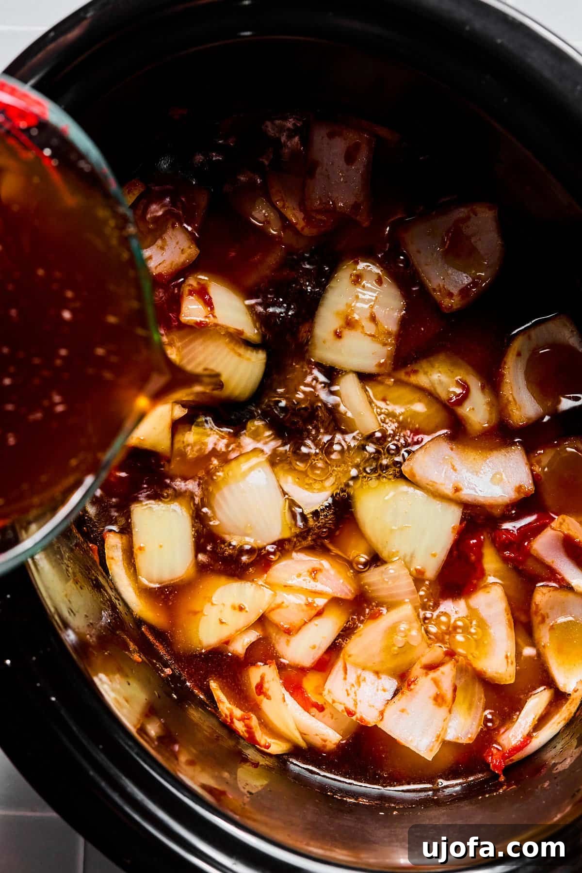Set It and Forget It Hearty Beef Stew 7 Beef broth being poured into a slow cooker over tomato paste, sautéed onions, and garlic, creating the stew's liquid base.