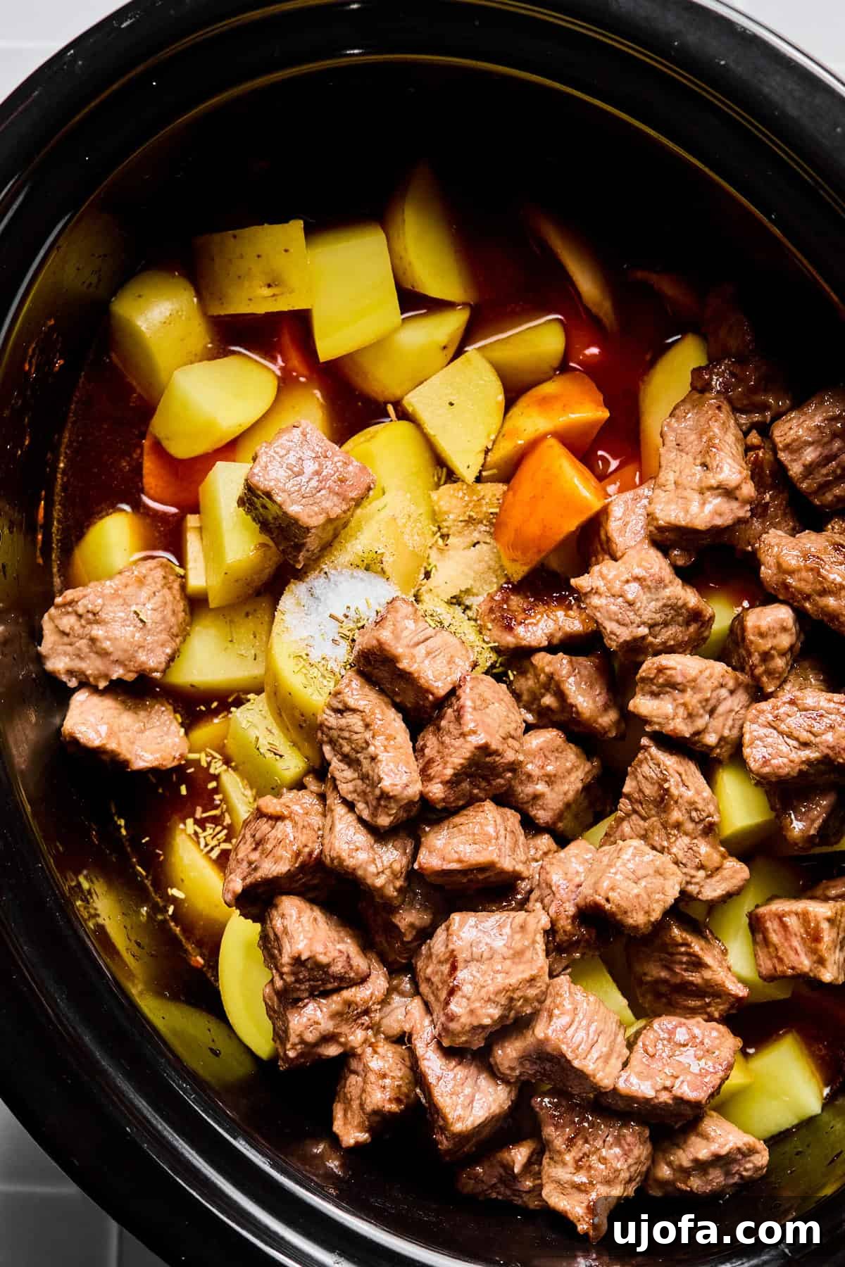 Set It and Forget It Hearty Beef Stew 8 All main ingredients – seared stew meat, carrots, potatoes, Worcestershire sauce, hot sauce, rosemary, thyme, salt, and pepper – combined in a slow cooker, ready for cooking.