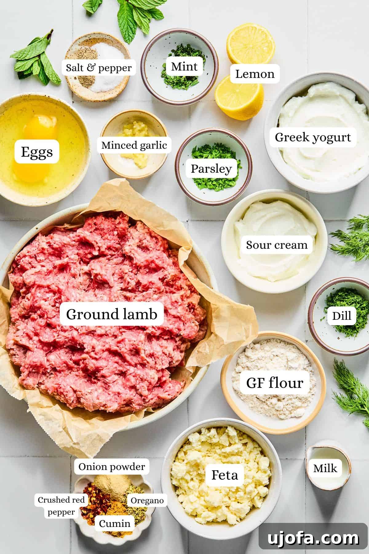 Greek lamb meatball ingredients laid out in nesting bowls on a white countertop.