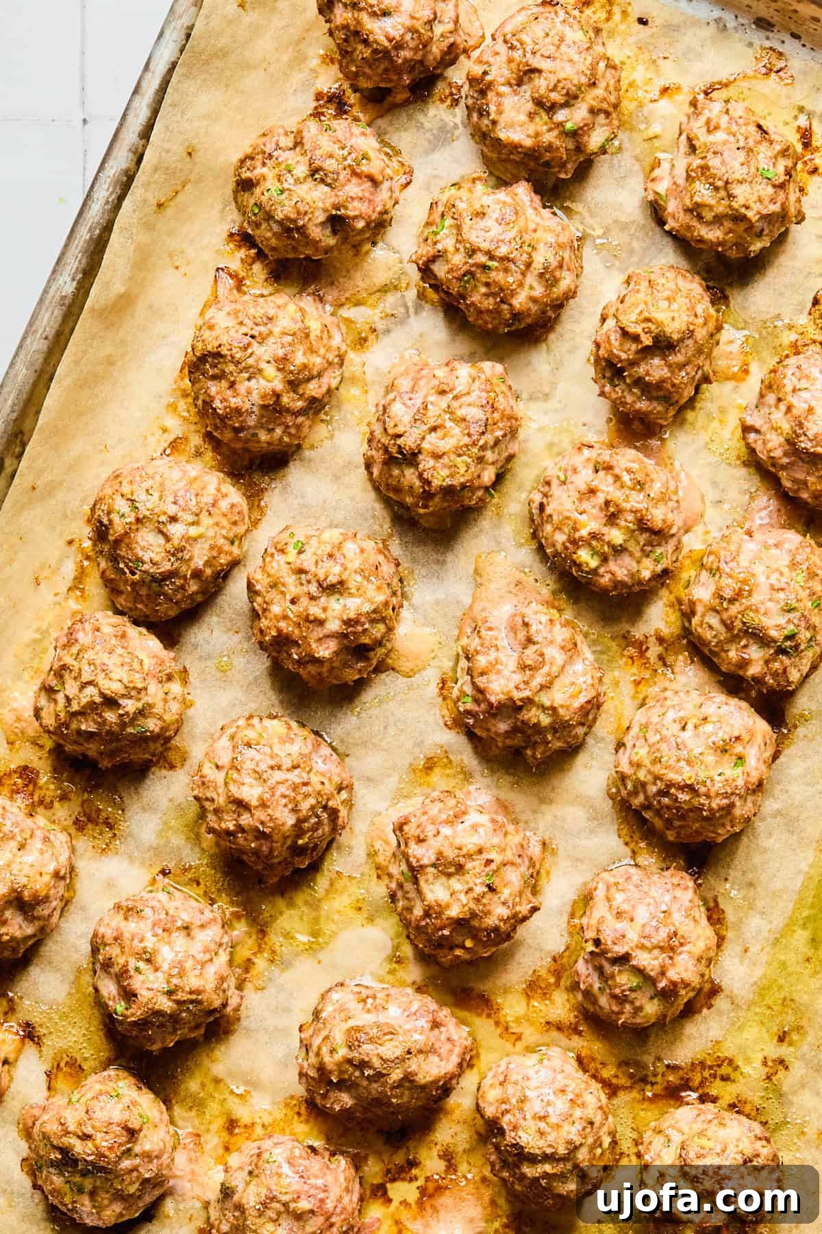 Lightly browned Greek lamb meatballs on a parchment-lined baking sheet.