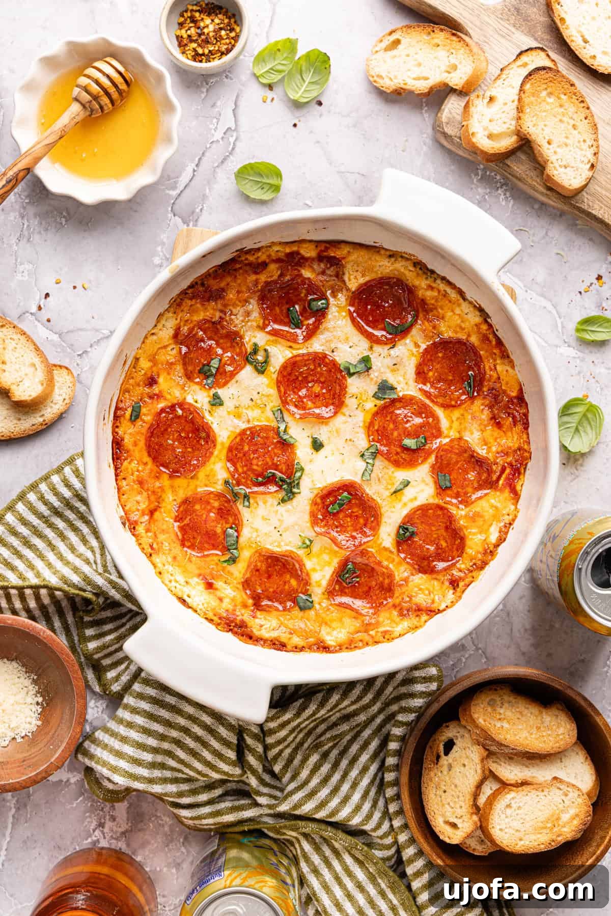 Ultimate Creamy Protein Pizza Dip 11 The glorious baked high protein pizza dip, presented in a round white baking dish, exquisitely topped with crispy pepperoni, perfectly melted cheese, a glistening hot honey drizzle, and fresh, vibrant basil. Ready to be devoured with various dipping vessels.