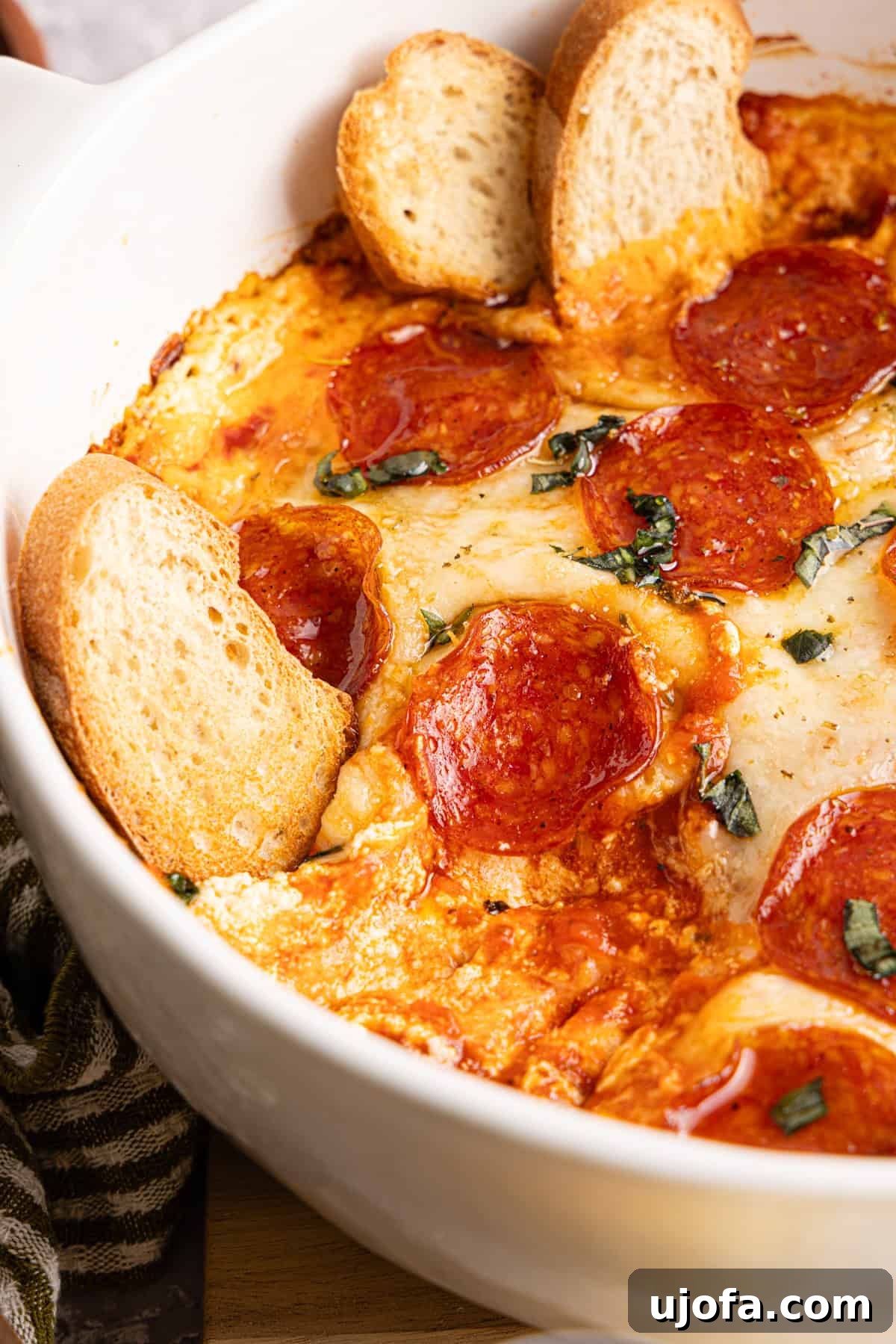 Ultimate Creamy Protein Pizza Dip 12 A tempting close-up shot of the baked high protein pizza dip in a round white dish, highlighting the bubbly, perfectly melted cheese, crisp pepperoni slices, glistening hot honey drizzle, and vibrant fresh basil leaves. Several slices of crusty bread are artfully embedded in the dip, ready for indulgent scooping.