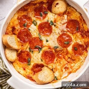 Creamy pizza dip in a casserole dish generously topped with pepperonis and basil, with baguette slices artfully placed for easy dipping.