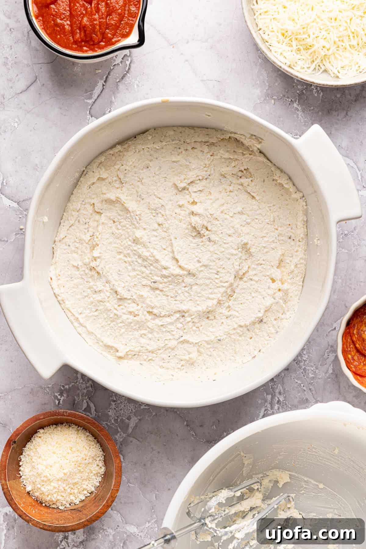 Ultimate Creamy Protein Pizza Dip 6 The smoothly blended high protein pizza dip mixture spread out evenly across the bottom of a ceramic baking dish, ready to receive the subsequent layers of pizza sauce, cheese, and toppings.
