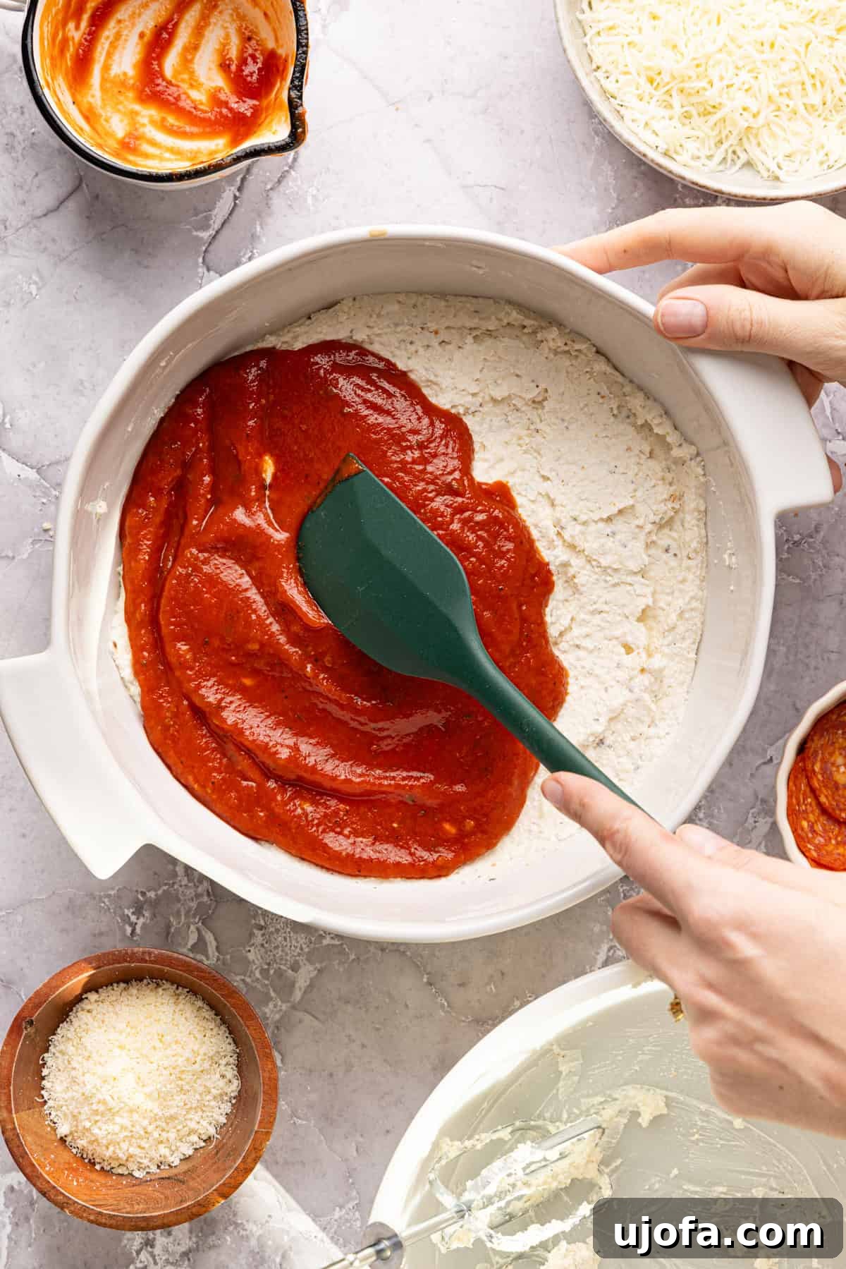 Ultimate Creamy Protein Pizza Dip 7 A hand gently spreading a rich, red pizza sauce over the evenly spread high protein pizza dip mixture in a ceramic baking dish, carefully creating the vibrant and iconic pizza flavor base.