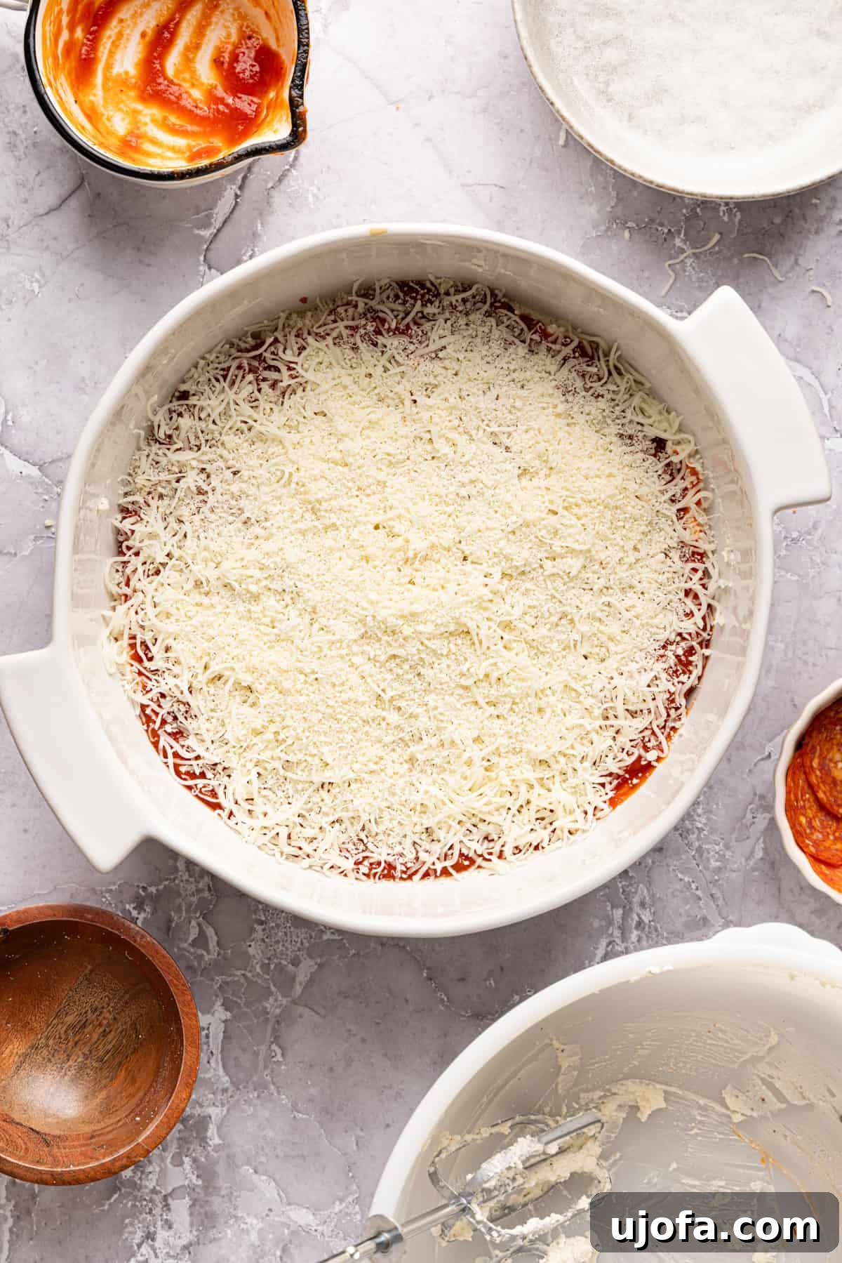 Ultimate Creamy Protein Pizza Dip 8 A generous sprinkling of shredded mozzarella and parmesan cheese covers the pizza sauce layer on the unbaked high protein pizza dip, meticulously preparing it for a perfectly melted, golden topping.