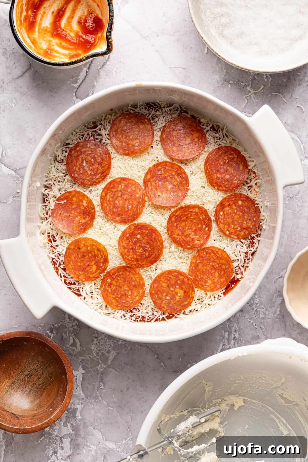 Ultimate Creamy Protein Pizza Dip 9 The unbaked high protein pizza dip beautifully assembled in a baking dish, adorned with layers of shredded cheese and perfectly arranged pepperoni slices on top, showcasing all the delicious elements ready for the oven's transformative heat.