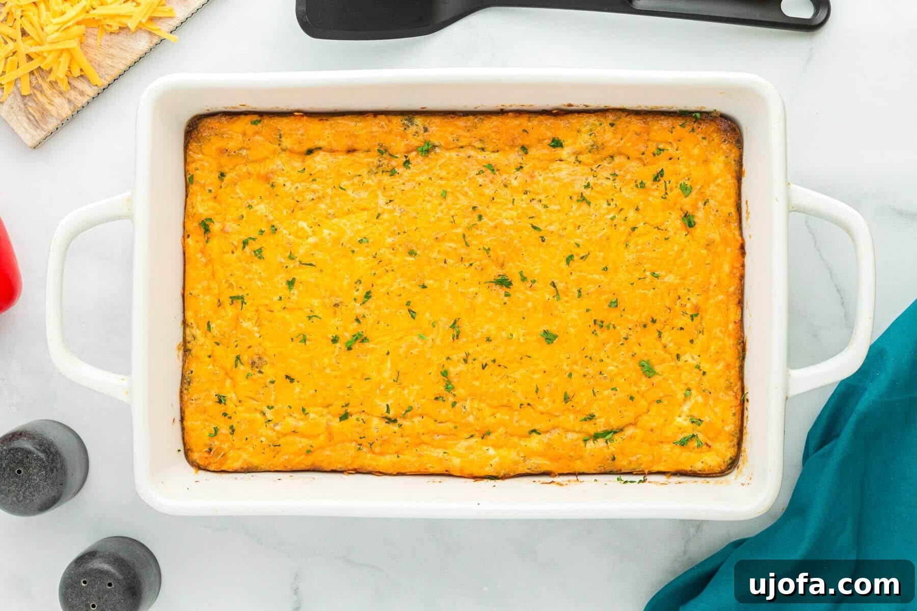 Yuletide Sausage Strata 5 An inviting overhead view of a golden-brown breakfast sausage and egg casserole, freshly baked in a white ceramic baking dish, showing off its cheesy topping and hearty ingredients.