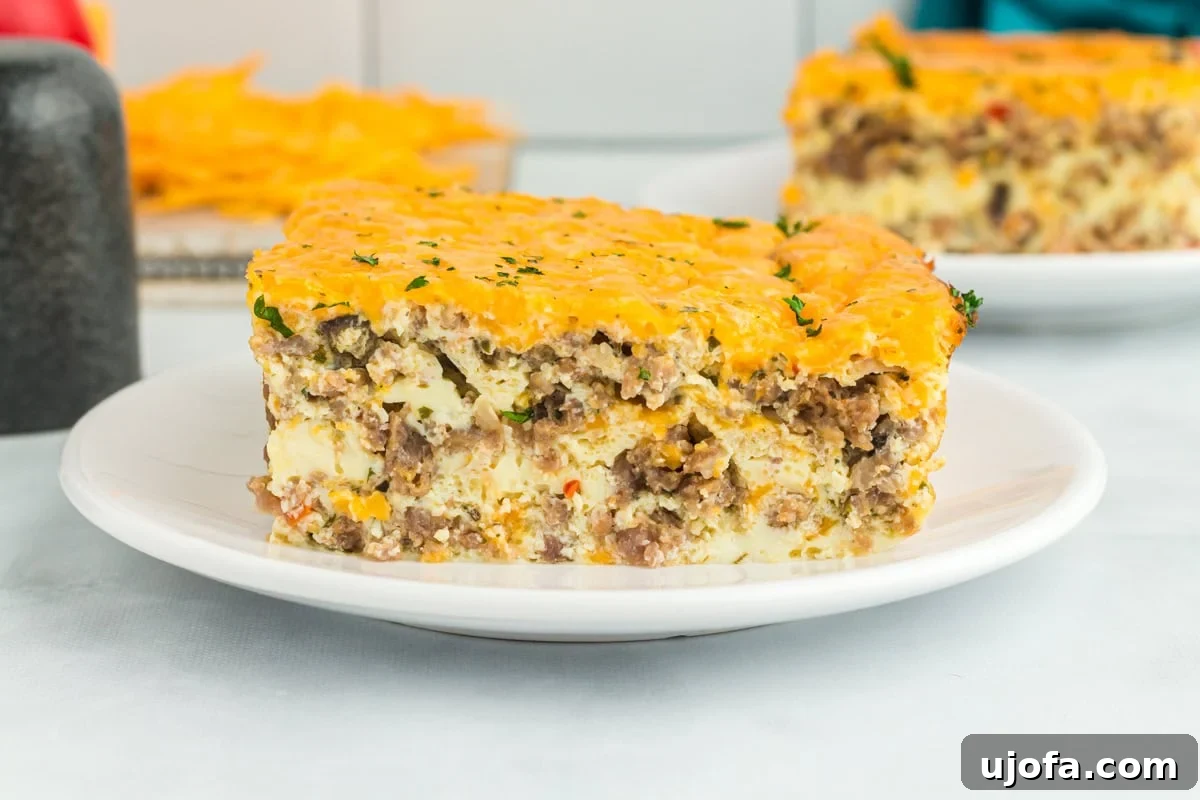 Yuletide Sausage Strata 7 A delectable slice of breakfast casserole, showcasing layers of sausage, eggs, and cheese, served elegantly on a white plate, highlighting its comforting textures and golden crust.