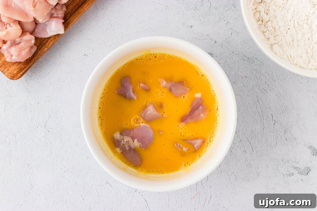Raw chicken pieces coated in egg wash, prepared for the dry flour mixture.