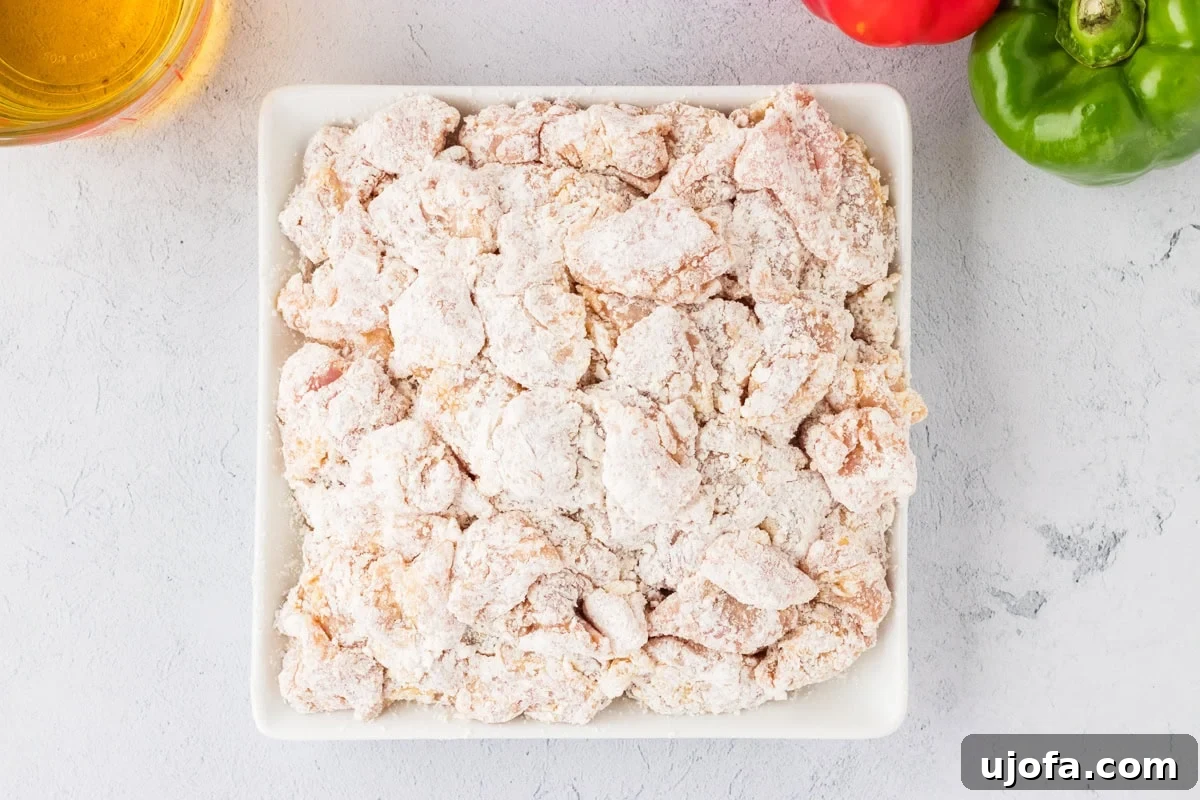 Flour-coated chicken pieces neatly arranged in a white square bowl, ready for frying.
