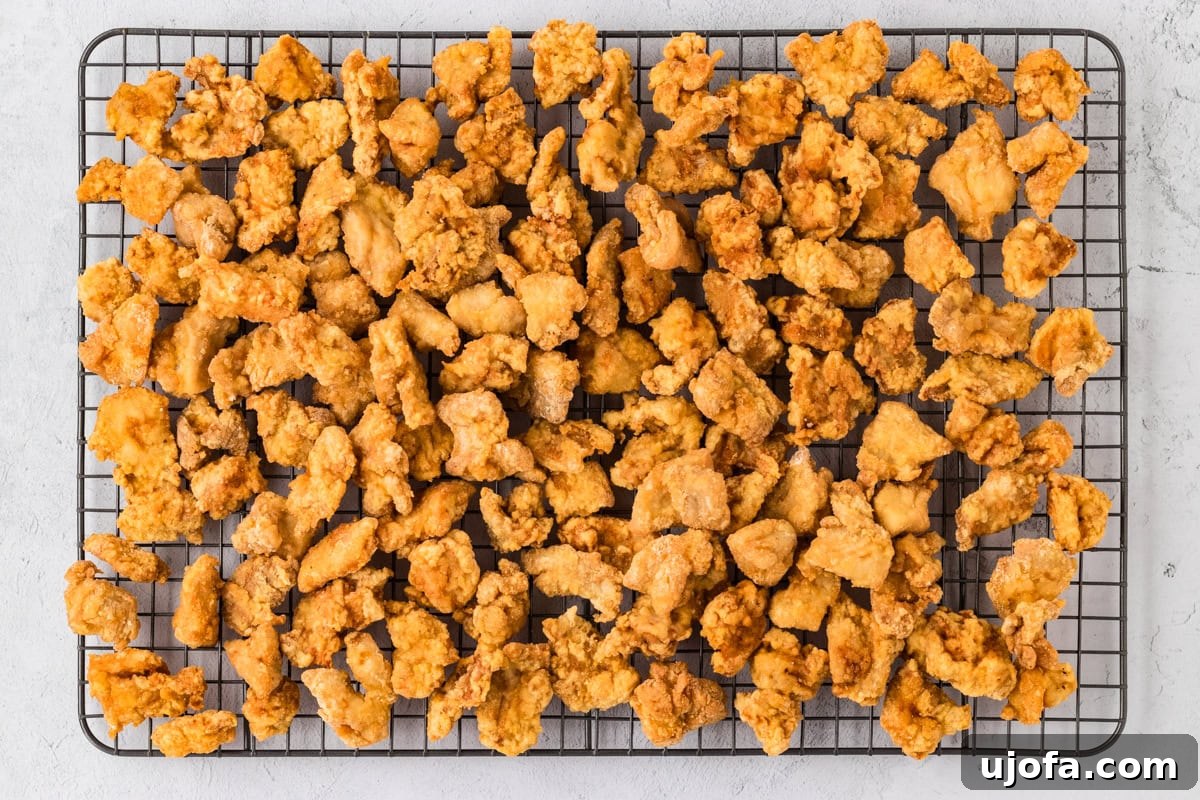 Cooked and coated chicken pieces resting on a wire drying rack after being fried.