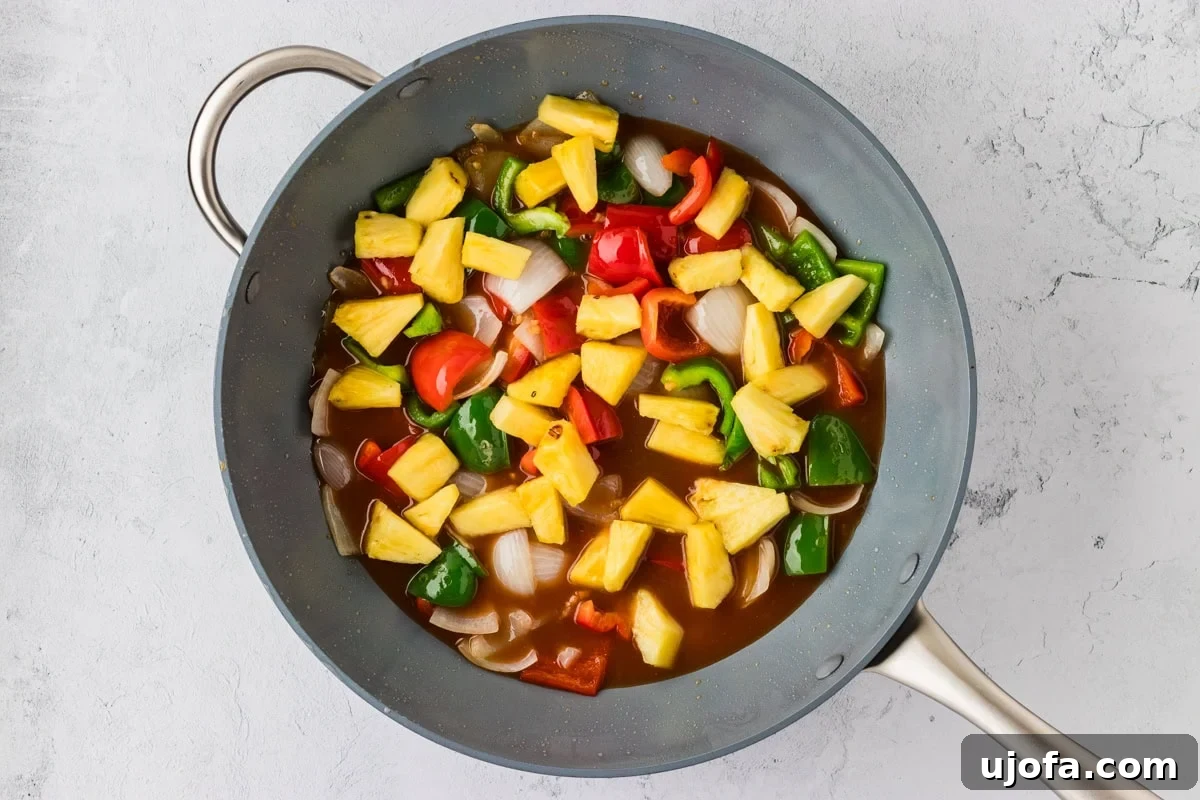 Overhead view of a wok with stir-fry vegetables and pineapple chunks simmering in the sweet and sour sauce.