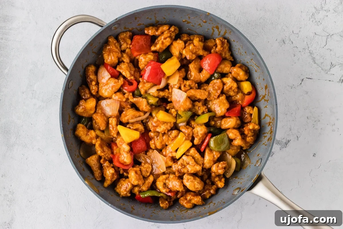 Gluten-free sweet and sour chicken mixed with stir-fry vegetables and sauce in a wok, ready to serve.