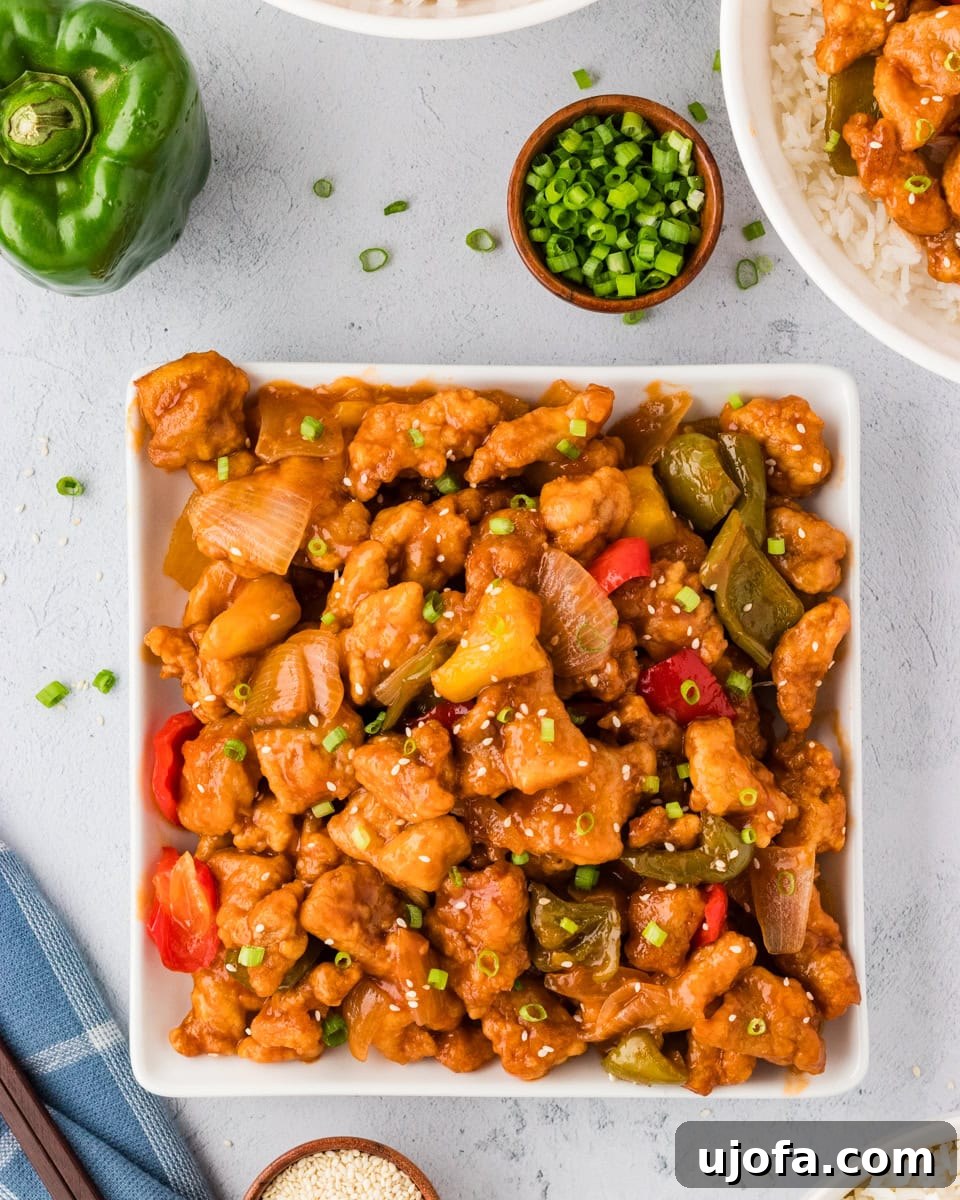 Overhead view of gluten-free sweet and sour chicken with vibrant bell peppers and pineapple in a square white bowl.
