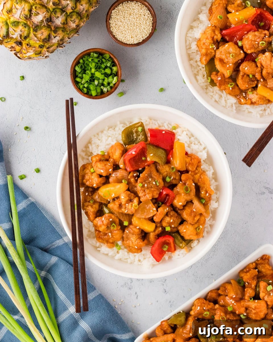 Overhead view of gluten-free sweet and sour chicken and stir-fry vegetables served over rice in a white bowl with chopsticks resting on the side.