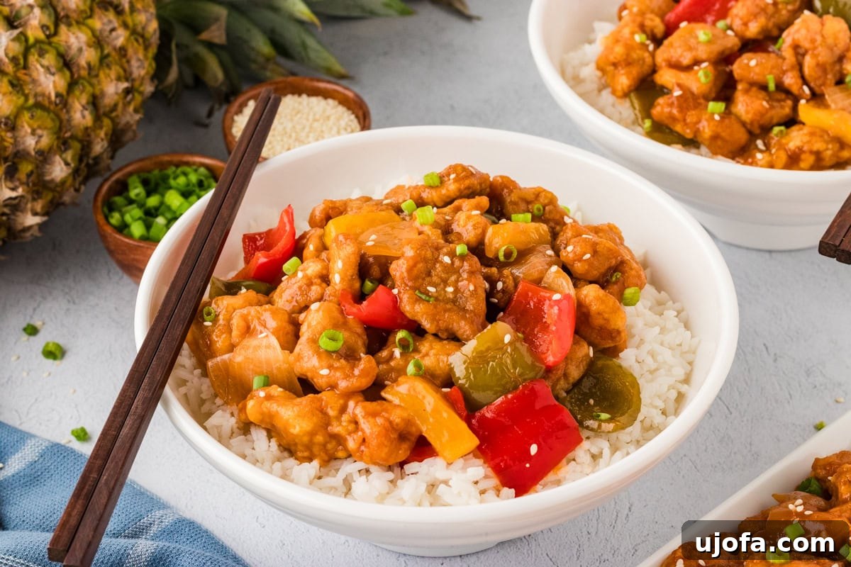 Close-up side view of gluten-free sweet and sour chicken served over white rice in a white bowl, with wooden chopsticks resting on the side.