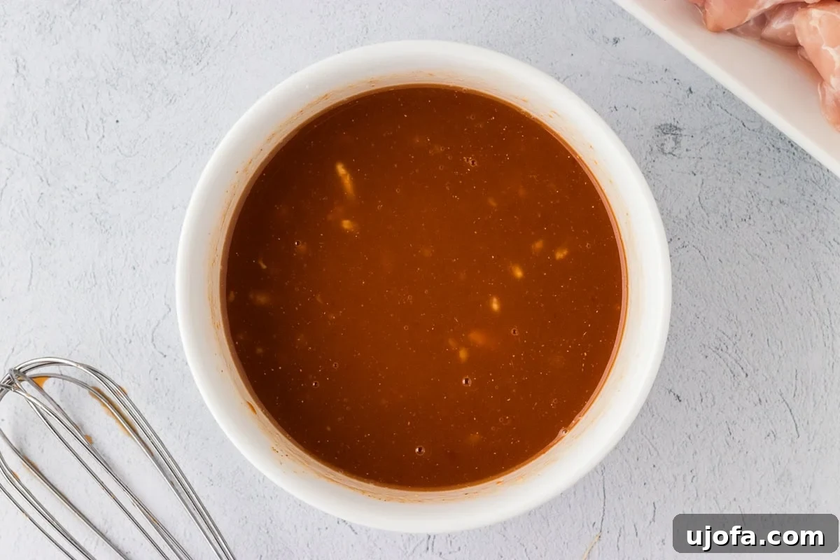 Ketchup, pineapple juice, and vinegar mixture for sweet and sour sauce in a white bowl, ready for whisking.