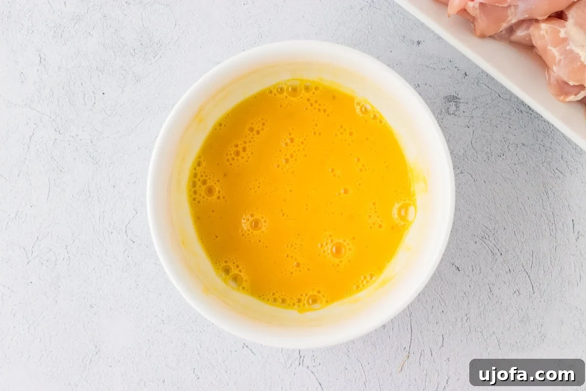 Whisked eggs in a small white bowl, prepared for coating chicken.