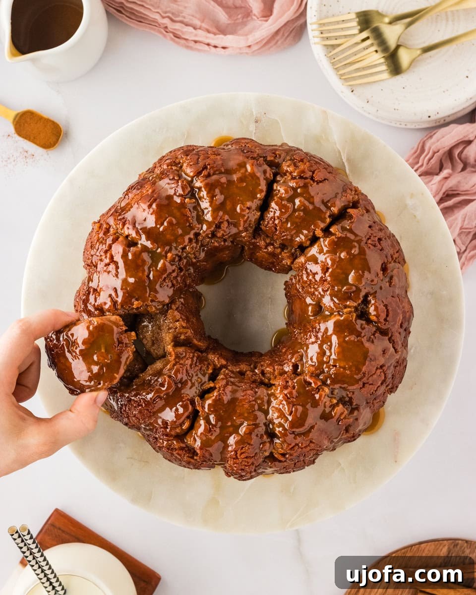 Gooey Gluten-Free Monkey Bread Indulgence 2 Hand reaching for a piece of golden-brown gluten-free monkey bread on a white cake platter, showcasing its sticky, caramelized texture.