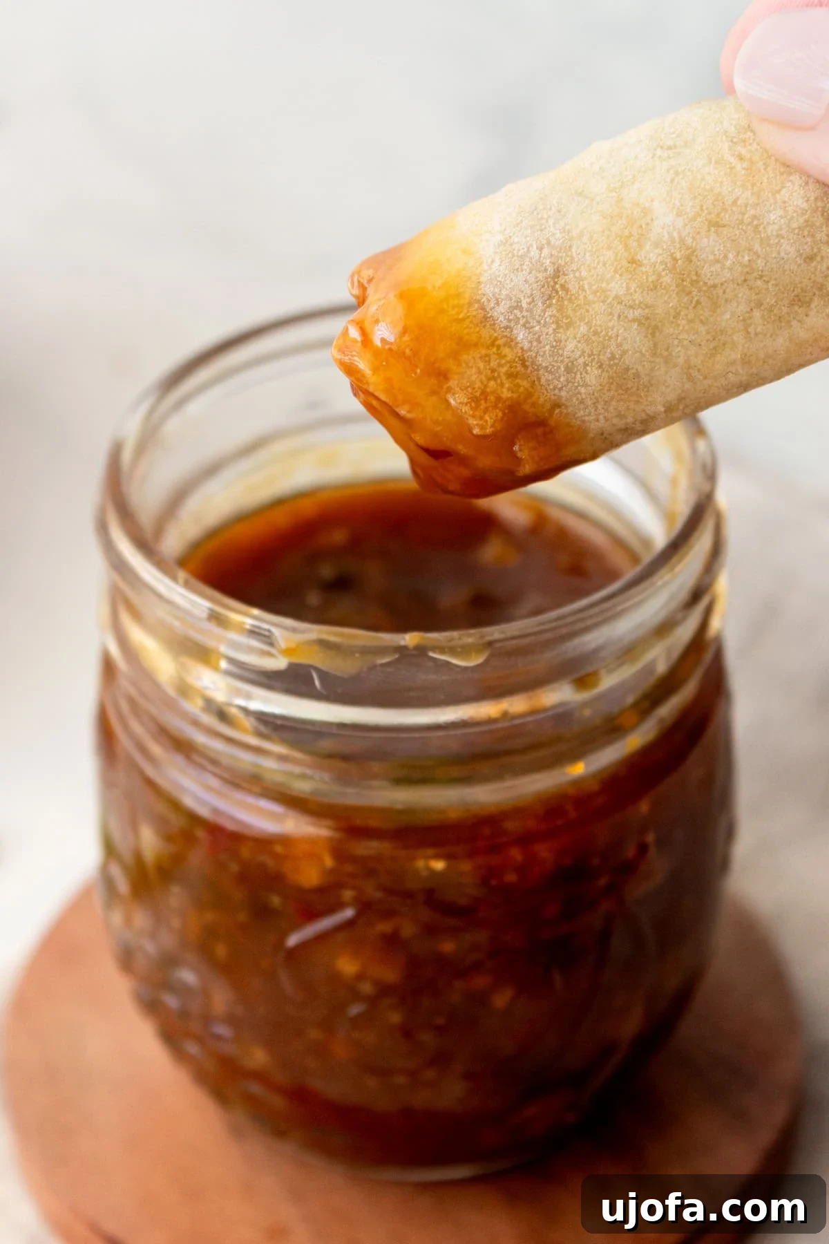 Golden Orange Reduction 4 A crispy spring roll being dipped into a jar of homemade orange reduction sauce with chopsticks.