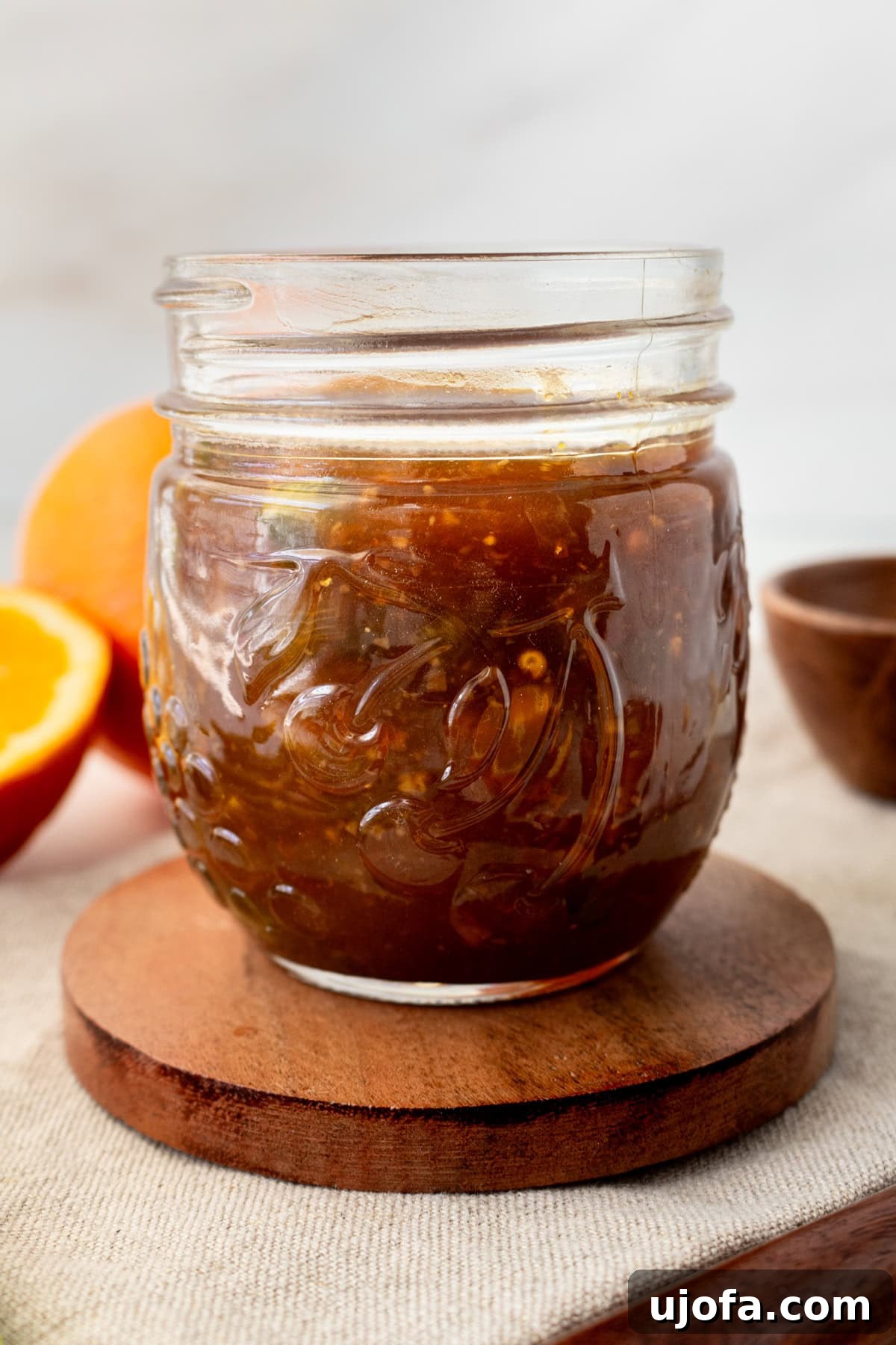 Golden Orange Reduction 5 A mason jar filled with glossy orange reduction sauce, resting on a wooden coaster.
