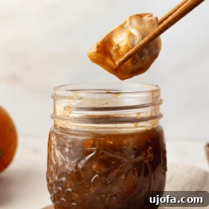 Golden Orange Reduction 6 A dumpling being dipped into a mason jar of orange reduction sauce with chopsticks.