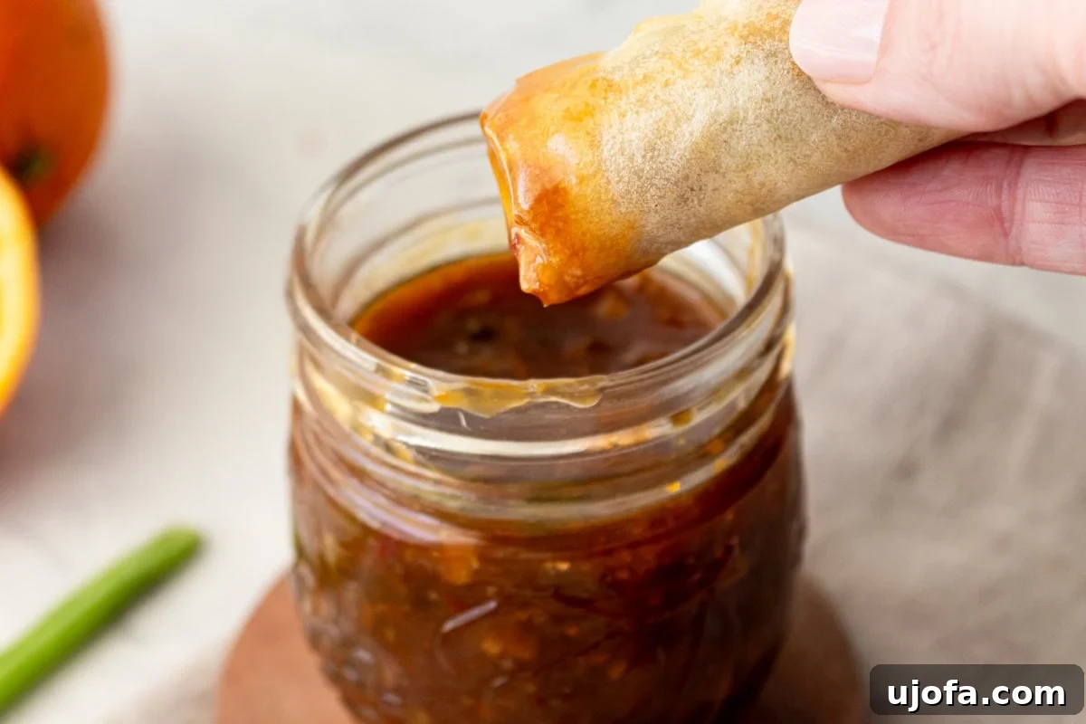 Golden Orange Reduction 7 A hand dipping a crispy spring roll into a mason jar filled with vibrant orange reduction sauce.